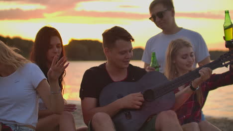 Los-Amigos-Tocan-La-Guitarra-Y-Cantan-Canciones-Alrededor-De-Una-Fogata-En-La-Fiesta-En-La-Playa.-Esta-Es-Una-Conmovedora-Tarde-De-Verano-Con-Los-Mejores-Amigos-Y-Cerveza.